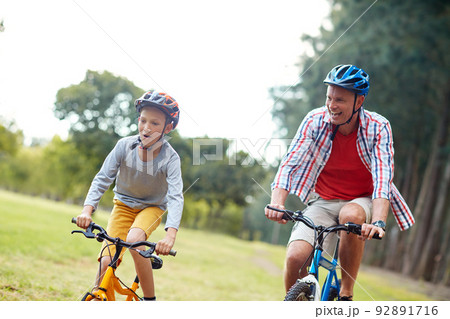 They love racing each other. Shot of a father and son riding bicycles in a park. 92891716