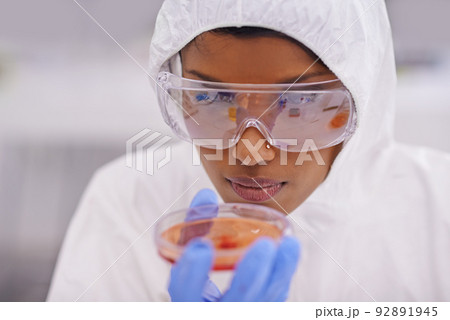 Careful observation. A young scientist in protective clothing examining a petri dish in her lab. 92891945