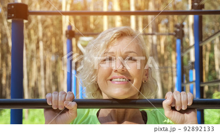 Mature woman does pull-ups smiling on sports ground closeup Mature woman does pull-ups smiling on sports ground closeup 92892133
