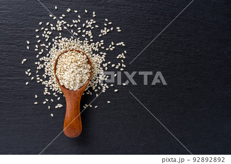 Raw sesame seeds in a wooden spoon over black slate background. 92892892