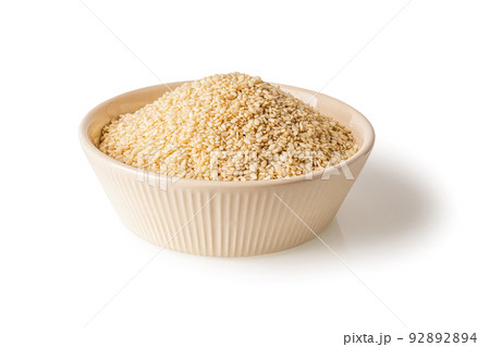White sesame seeds in a beige bowl isolated on a white background.  92892894