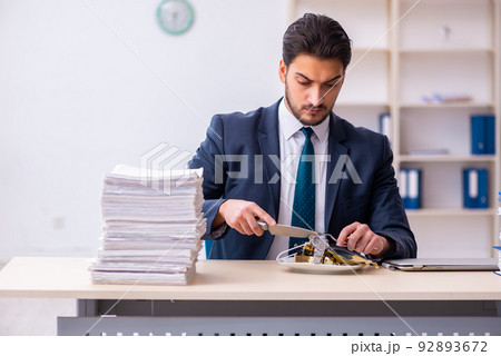 Young businessman employee eating alarm-clock Young businessman employee eating alarm-clock 92893672