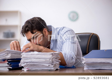 Young male employee and too much work in the office Young male employee and too much work in the office 92893681