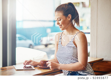 Coffee and wifi - the best way to spend the day. Shot of a young woman using her digital tablet in a coffee shop. 92893877