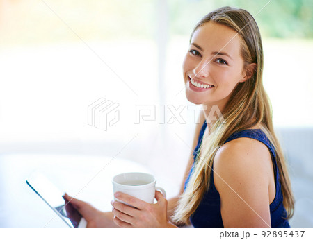 I have all the company I need right here..... Shot of a young woman using her digital tablet while having cup of coffee. I have all the company I need right here..... Shot of a young woman using her digital tablet while having cup of coffee. 92895437