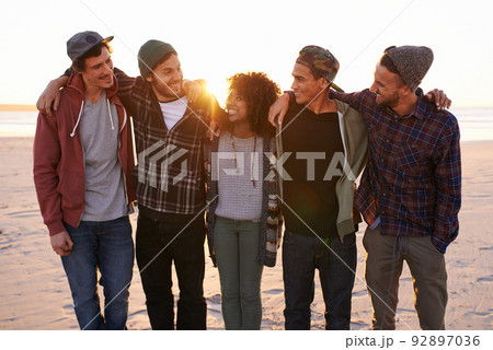 Friends make the world a better place. Shot of a group of friends walking along a beach at sunset. 92897036