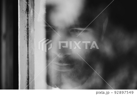 Blurred viewpoint. Closeup of a thoughtful young man seen through a window. Blurred viewpoint. Closeup of a thoughtful young man seen through a window. 92897549