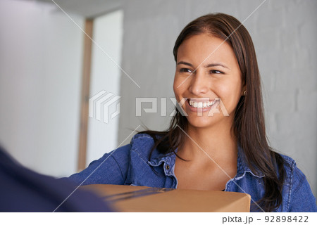 Excited to get settled in. A beautiful young woman smiling at the camera as she takes a box from a mover. 92898422