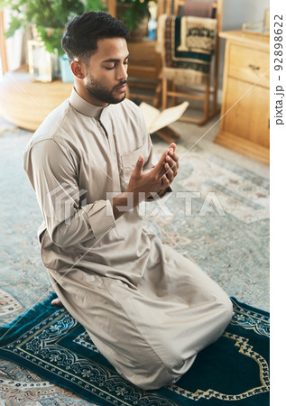 Prayer is devotion. Shot of a young muslim man praying in the lounge at home. Prayer is devotion. Shot of a young muslim man praying in the lounge at home. 92898622