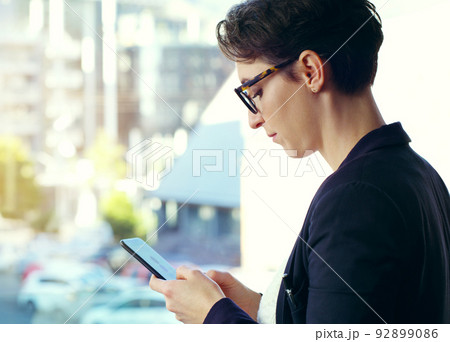Sending out a work update. Cropped shot of an attractive young businesswoman using a mobile phone while standing on her office balcony. Sending out a work update. Cropped shot of an attractive young businesswoman using a mobile phone while standing on her office balcony. 92899086