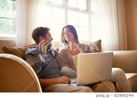 Smiling together over social media. Shot of a happy young couple using a laptop while sitting on the sofa. 92900244
