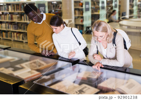 Teacher and adult students view rare books in a library showcase Teacher and adult students view rare books in a library showcase 92901238
