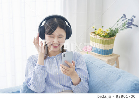 自宅でヘッドホンをしてスマホで音楽を聴く女性 自宅でヘッドホンをしてスマホで音楽を聴く女性 92901700