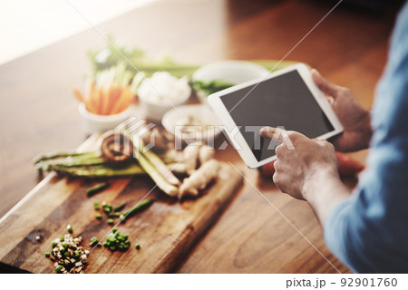 Closeup of hands of man holding a tablet to research healthy recipes, watch cooking tutorial videos and scrolling online for meal ideas while making dinner, lunch or breakfast. Man browsing on app 92901760