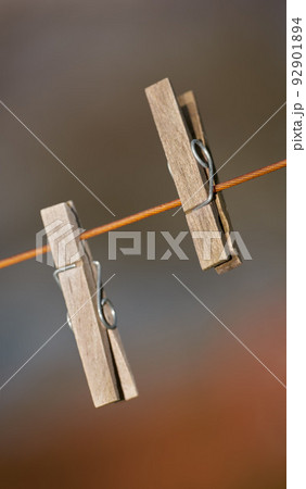 Closeup of two clothing pegs on a washing line outside against a blurred background. Wooden clothespins used to clip and hang clean laundry in the sun to dry as part of household and domestic chores Closeup of two clothing pegs on a washing line outside against a blurred background. Wooden clothespins used to clip and hang clean laundry in the sun to dry as part of household and domestic chores 92901894