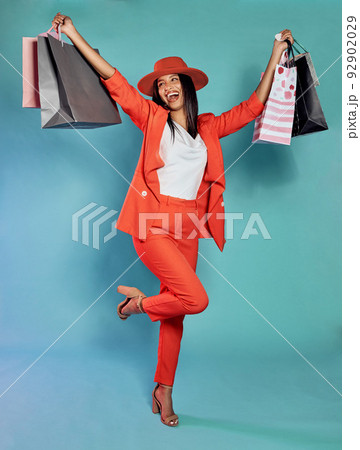 Excited and trendy woman with shopping bags after retail therapy, spending and buying clothes. Stylish, edgy and funky model holding gifts and wearing colorful, fashionable red suit while happy 92902029