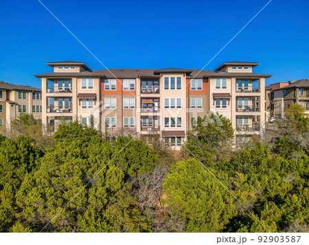 Austin, Texas- Apartment building with balconies and picture windows on top of a slope with trees Austin, Texas- Apartment building with balconies and picture windows on top of a slope with trees 92903587