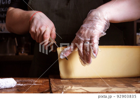 Saleswoman cutting cheese for sale. Cheese shop. 92903835