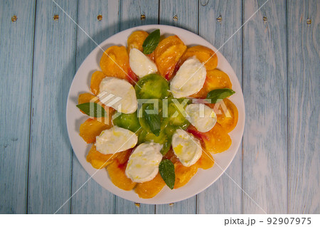 Green and Orange tomato and mozzarella salad with basil leaves and olive oil 92907975