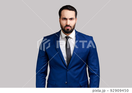 Portrait of bearded businessman looking at camera with angry face, having aggressive facial expression, wearing official style suit. Indoor studio shot isolated on gray background. 92909450