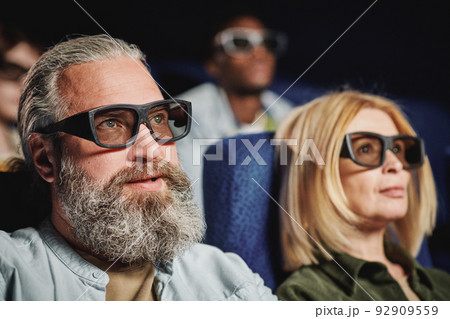 Selective focus shot of of handsome mature man with beard on face wearing 3D eyeglasses watching movie in cinema 92909559