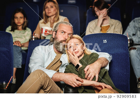 Horizontal shot of beaded Caucasian man comforting his wife while watching tragedy movie at cinema 92909583