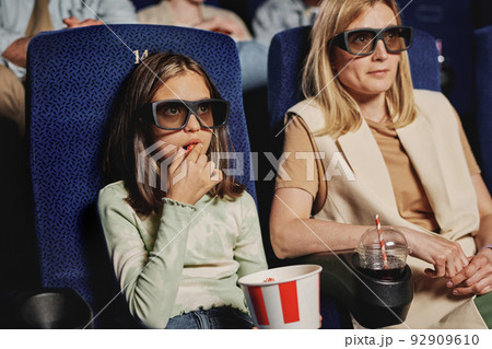 Portrait of stylish Caucasian woman and her daughter wearing 3D eyeglasses watching movie at cinema Portrait of stylish Caucasian woman and her daughter wearing 3D eyeglasses watching movie at cinema 92909610