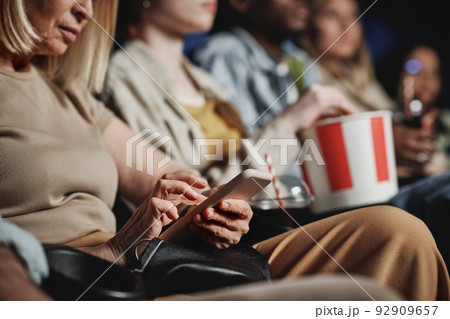 Selective focus of mature Caucasian woman surfing Internet on smartphone while watching movie at cinema 92909657