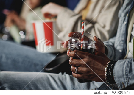 Selective focus shot of unrecognizable Black man holding plastic cup with cola drink at cinema 92909675
