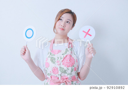 ○✖️の札を持つエプロン姿の若い女性 92910892