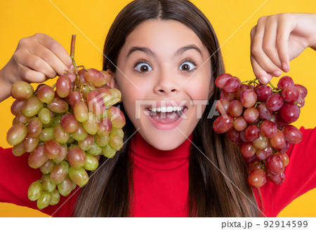 glad amazed girl hold bunch of grapes on yellow background 92914599