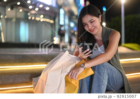 Beautiful young woman sitting on stairs in the night city and typing text message on her mobile phone Beautiful young woman sitting on stairs in the night city and typing text message on her mobile phone 92915007