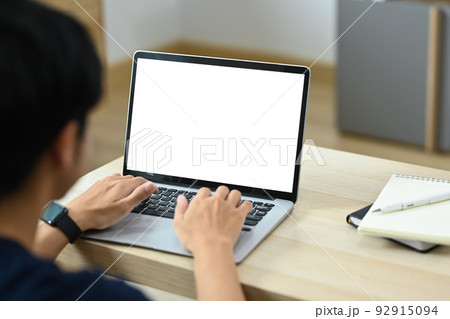 Over shoulder view of male freelancer sitting in bright living room and working online, searching information online on laptop computer 92915094