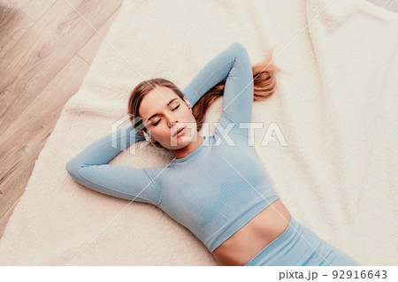 Top view portrait of relaxed woman listening to music with headphones lying on carpet at home. She is dressed in a blue tracksuit. Top view portrait of relaxed woman listening to music with headphones lying on carpet at home. She is dressed in a blue tracksuit. 92916643