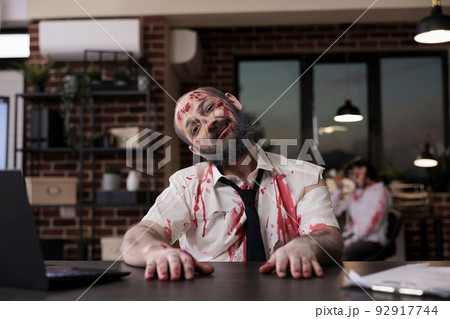 Portrait of walking dead corpse in office working on startup business with laptop, creepy evil monster sitting at desk. Brain eating horrific zombie with bloody wounds and dirty scars, eerie walker. Portrait of walking dead corpse in office working on startup business with laptop, creepy evil monster sitting at desk. Brain eating horrific zombie with bloody wounds and dirty scars, eerie walker. 92917744