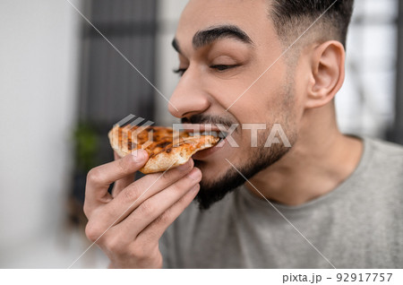 Face of man biting pizza sideways to camera Face of man biting pizza sideways to camera 92917757