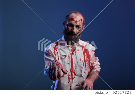 Portrait of halloween zombie with scars and bloody wounds posing in front of camera, dangerous undead corpse with scary scratches and creepy face in studio. Doomsday cruel monster devil. 92917828