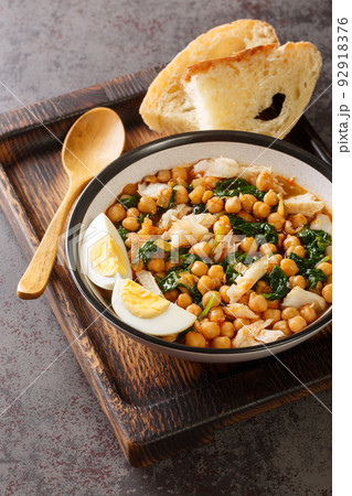 Potaje de Vigilia Spanish chickpea stew with cod and spinach close-up in a bowl on the wooden tray. Vertical 92918376