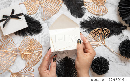Hands with Blank card and envelope near black feathers and golden leaves top view Hands with Blank card and envelope near black feathers and golden leaves top view 92920144