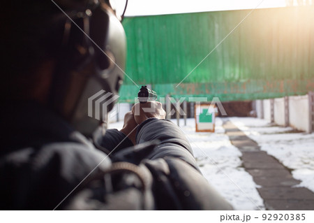 A man with headphones is aiming at the target. Tyre outside the door. Winter. Sports entertainment, firearms. 92920385