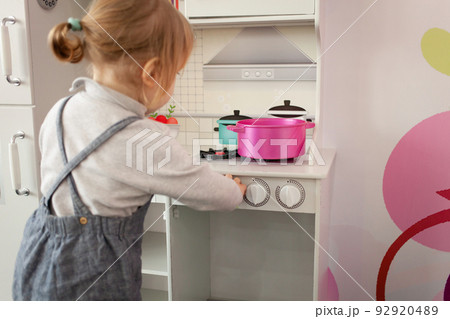 A small two-year-old girl plays with toys in the playroom. Development Centre, Kindergarten Baby plays with pot in kitchen 92920489