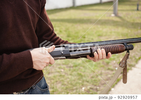 A young man charges a pump-action shotgun with a Ammo. 12 caliber. Tyre outdoor. A man in headphones and goggles is preparing to shoot. Firearms for sports shooting, hobby. A young man charges a pump-action shotgun with a Ammo. 12 caliber. Tyre outdoor. A man in headphones and goggles is preparing to shoot. Firearms for sports shooting, hobby. 92920957