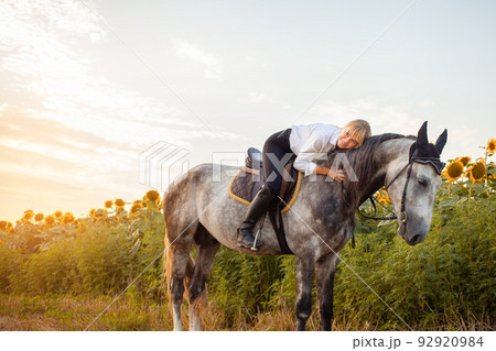 a woman rides a gray horse in a field at sunset. Freedom, beautiful background, friendship and love for the animal. Sports training equestrian, rental and sale of horses, hiking, riding, walking. Hugs 92920984