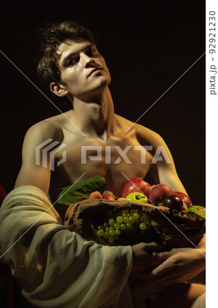 Creative remake of painting boy with a basket of fruit. Young handsome man over dark vintage background. Italian baroque style, art, creativity, vintage 92921230