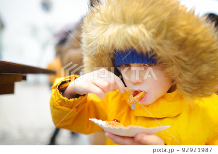 Child eating traditional Poland street food oscypek on Christmas market in Krakow. Oscypek is a grilled cheese of salted sheep milk with different ingredients as bacon or jams. Local cuisine. 92921987