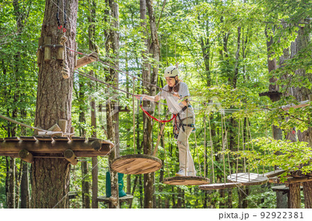 Happy women girl female gliding climbing in extreme road trolley zipline in forest on carabiner safety link on tree to tree top rope adventure park. Family weekend children kids activities concept Happy women girl female gliding climbing in extreme road trolley zipline in forest on carabiner safety link on tree to tree top rope adventure park. Family weekend children kids activities concept 92922381