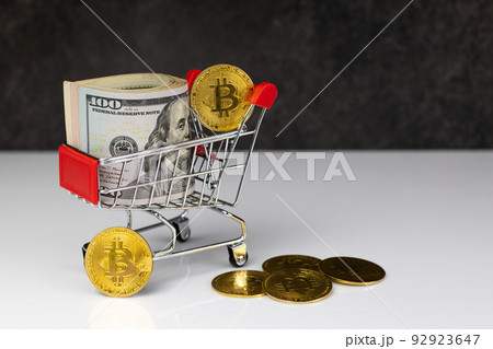 Bitcoin and roll of dollars in shopping cart or basket on dark grey background. Buy or Sell. The concept of the impact of virtual currency on the economy Bitcoin and roll of dollars in shopping cart or basket on dark grey background. Buy or Sell. The concept of the impact of virtual currency on the economy 92923647