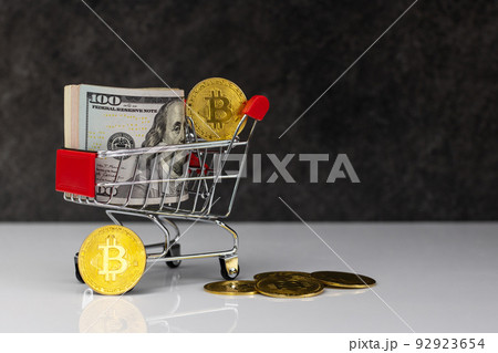 Bitcoin and roll of dollars in shopping cart or basket on dark grey background. Buy or Sell. The concept of the impact of virtual currency on the economy 92923654