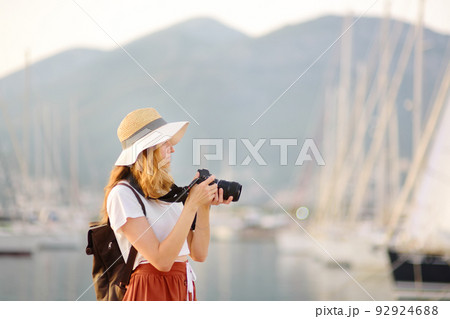 Charming young tourist woman taking a picture on the Mediterranean coast. Attractive red-haired girl photographer with a camera on the background of sea and yachts. Charming young tourist woman taking a picture on the Mediterranean coast. Attractive red-haired girl photographer with a camera on the background of sea and yachts. 92924688