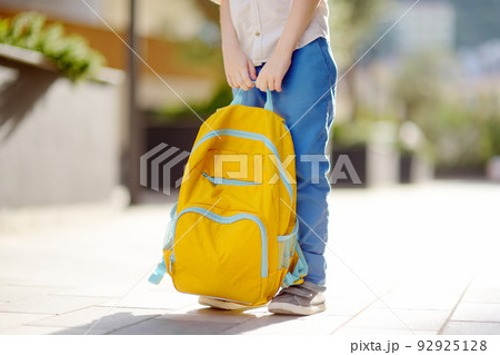 Little student with a backpack near school building. Close-up of child legs, hands and schoolbag of boy standing on staircase of schoolhouse. Back to school concept. 92925128
